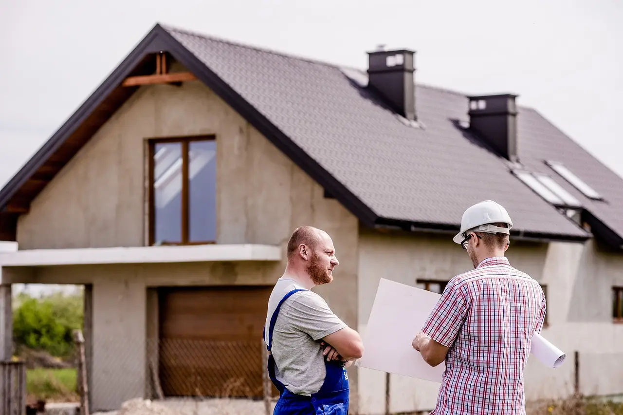 Zwei Handwerker mit Bauplan vor einem Einfamilienhaus im Rohbau