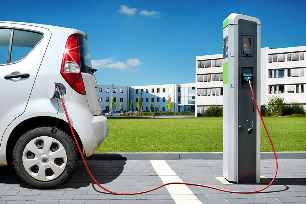 Elektroauto lädt an einer Ladesäule auf einem Parkplatz, rotes Ladekabel, im Hintergrund Bürogebäude und Rasen