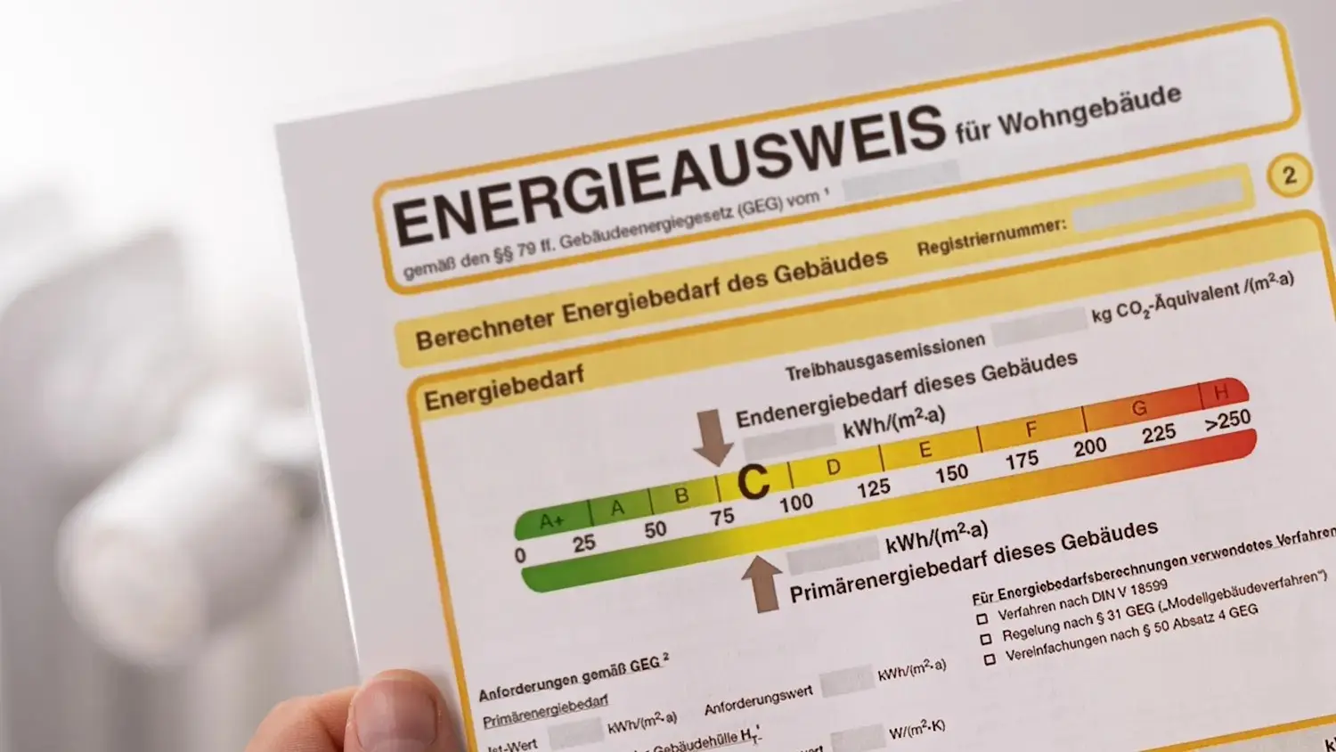 Hand hält die erste Seite eines Energieausweises für Wohngebäude mit Effizienzskala von A+ bis H