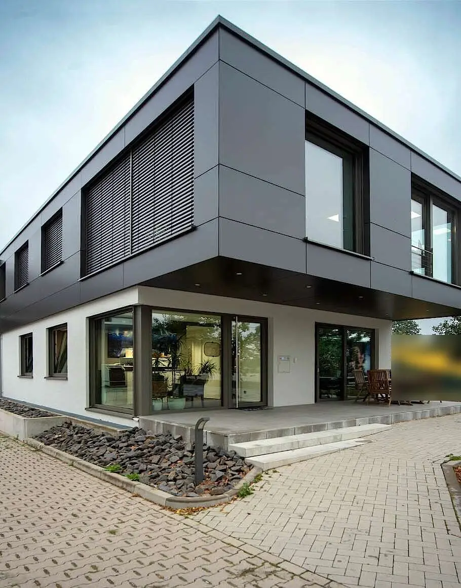 Modernes zweigeschossiges Gewerbegebäude mit Flachdach, dunkler Plattenfassade im Obergeschoss, großen Fensterfronten und Terrasse im Erdgeschoss