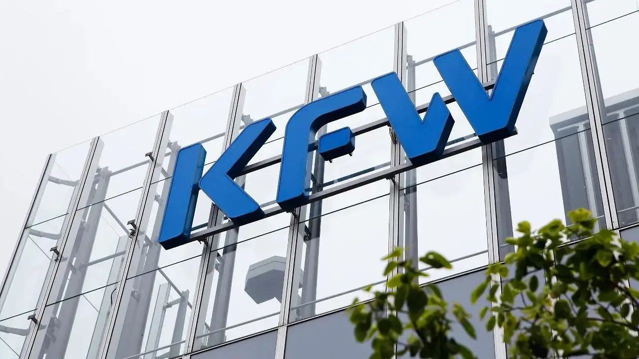 Schriftzug KfW an der Glasfassade eines Bürogebäudes, davor grüne Blätter