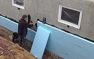 Handwerker bringt Dämmplatten an der freigelegten Kelleraußenwand an