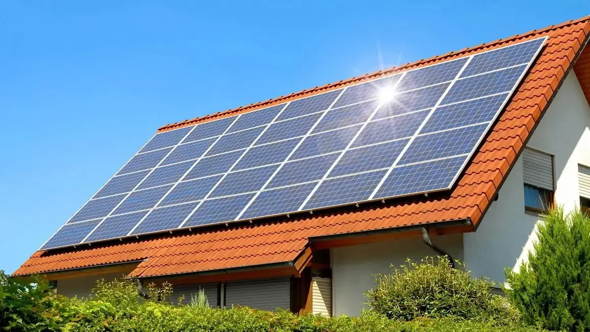 Photovoltaikanlage auf dem roten Ziegeldach eines Einfamilienhauses bei blauem Himmel und Sonnenschein