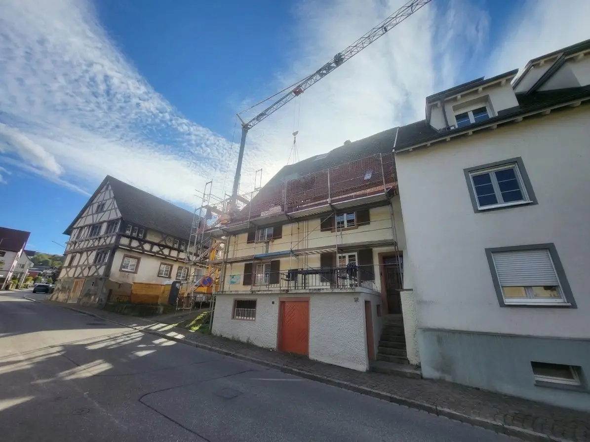 Eingerüstetes historisches Wohnhaus während der Dachsanierung, darüber ein Baukran; links daneben ein Fachwerkhaus