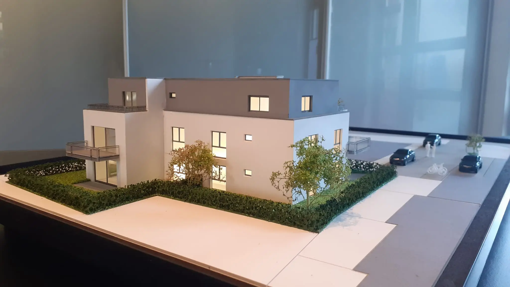 Architekturmodell des geplanten Mehrfamilienhauses in Lörrach: zwei Vollgeschosse und ein zurückgesetztes Dachgeschoss mit Flachdach, Balkone, Garten mit Hecke und Stellplätze an der Straße