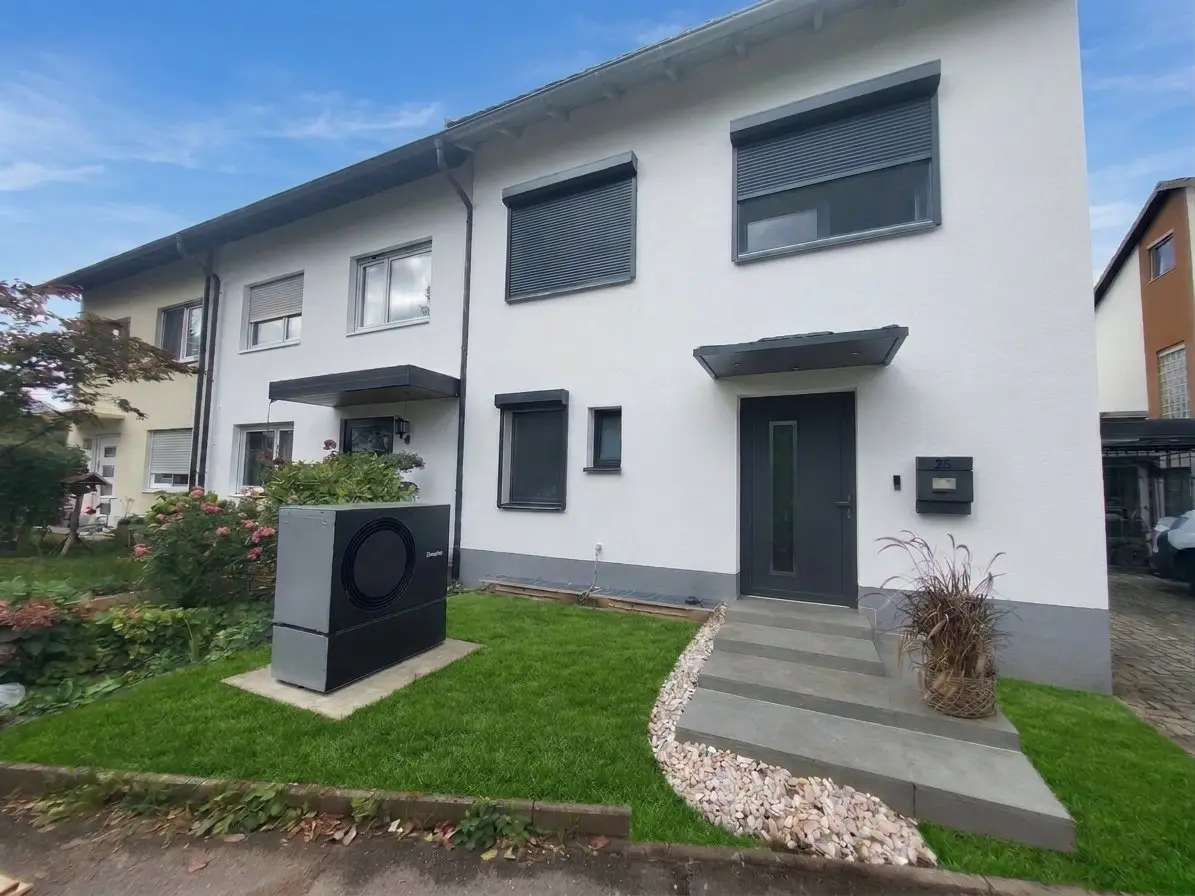 Saniertes Reihenendhaus mit weißer gedämmter Fassade, anthrazitfarbenen Fenstern mit Rollläden, neuer Haustür und Luft-Wasser-Wärmepumpe im Vorgarten